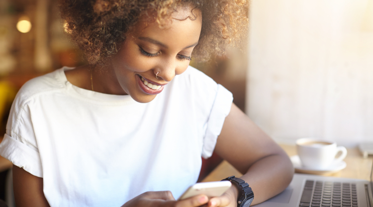 African American woman sitting in a cafe, smiling while scrolling through her phone