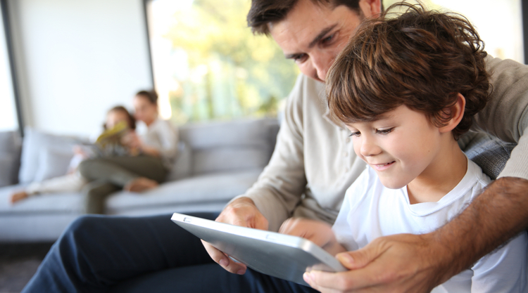 Father and son at home spending time looking at tablet together