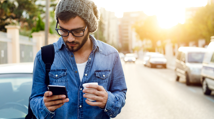 Man walking outside holding coffee while scrolling phone