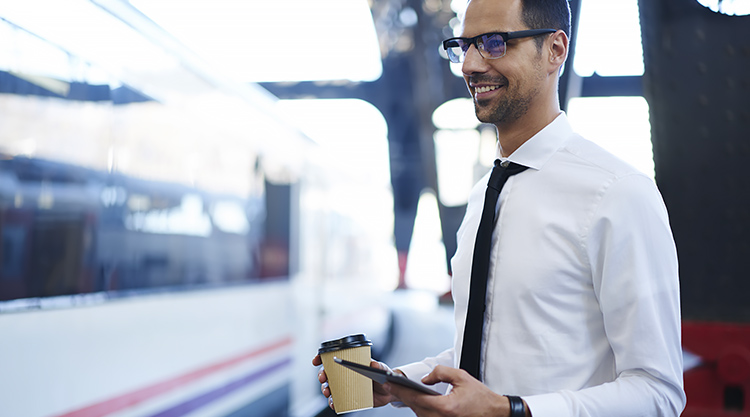 A man holding a cup of coffee and cell phone while standing outside in front of a train