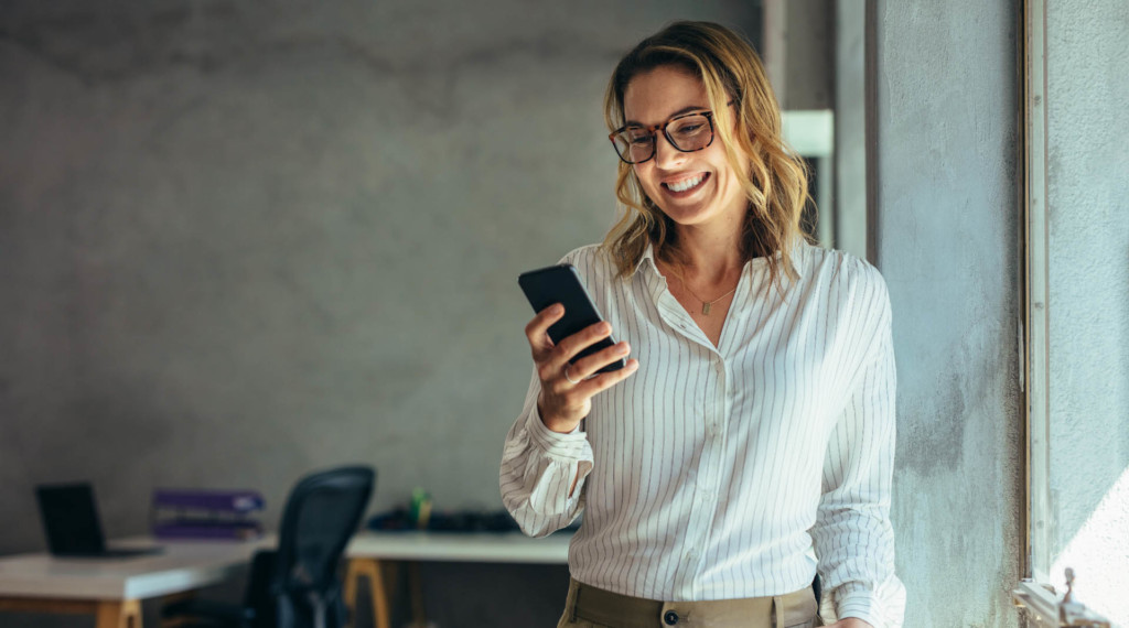 A smiling woman holding a cell phone in a work office