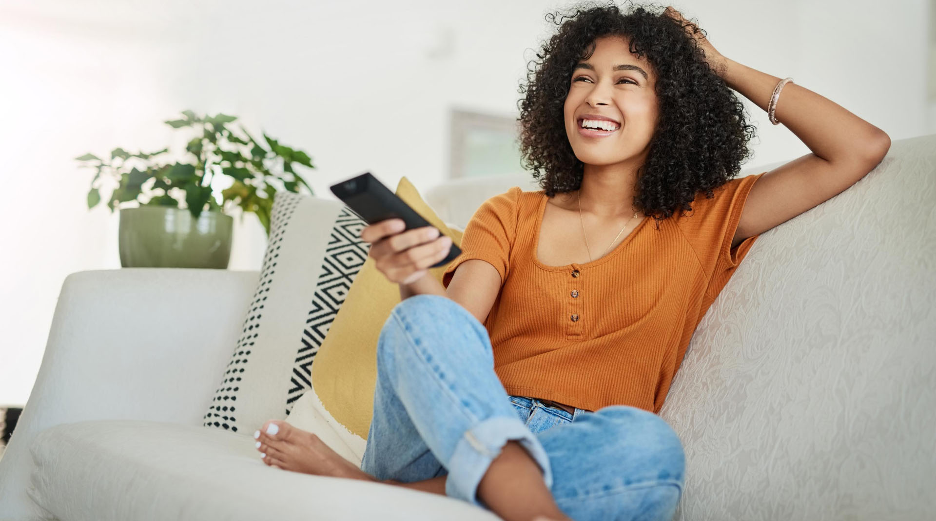 A smiling young woman holding a TV remote control while sitting on a couch