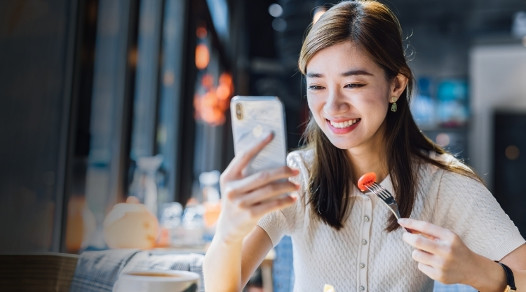 Smiling woman holding her cellphone and eating a peace of carrot in a restaurant