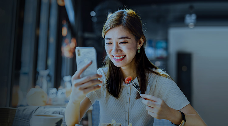 Smiling young woman looking at cellphone and eating at a restaurant