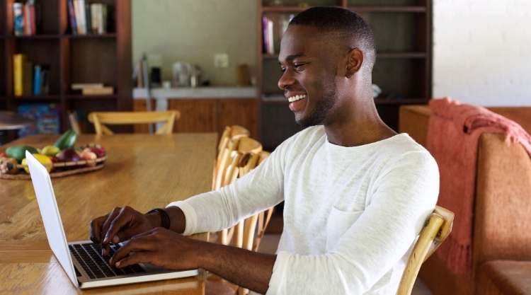 Smiling adult man typing on his laptop while sitting in his living room