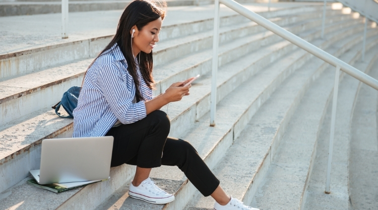 Woman sitting on staircase with a laptop next to her and holding a cellphone