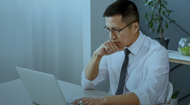 Adult man sitting at a desk and staring pensively at a laptop screen