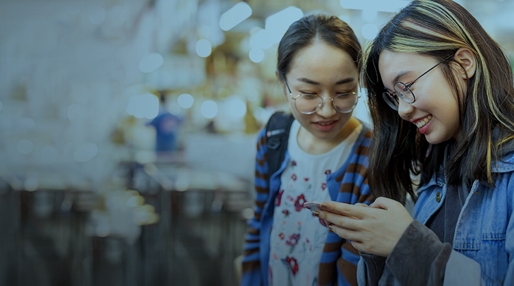 Two young girls looking at a cellphone while walking through a city