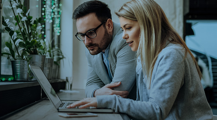 Adult woman typing on her laptop and adult man next to her looking over