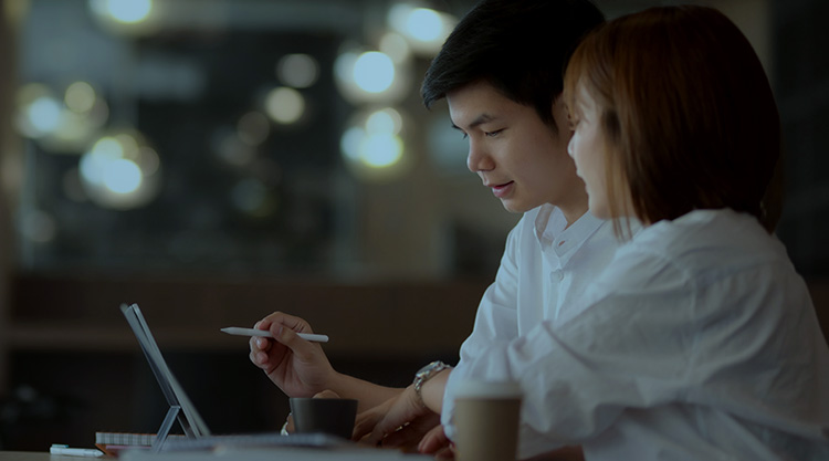 A student holding a tablet pen and a young woman sitting next to him looking at the screen in front of him