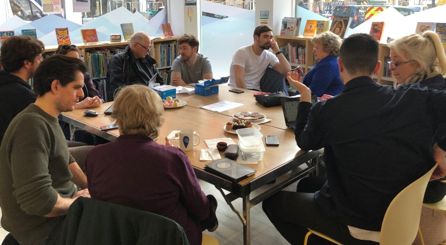 Ten adults seated in a children's library with desserts and snacks placed in front of them