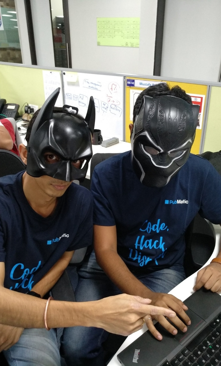Two seated men wearing superhero masks and typing on their laptop