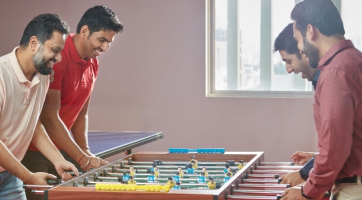 Four men laughing and playing foosball together in a game room