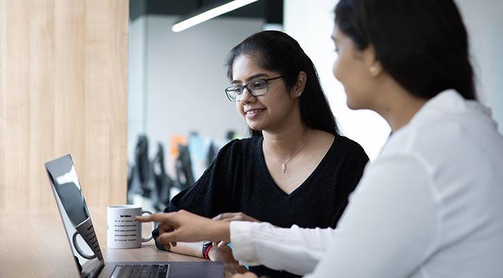Two adult women in the office having a discussion in front of a laptop