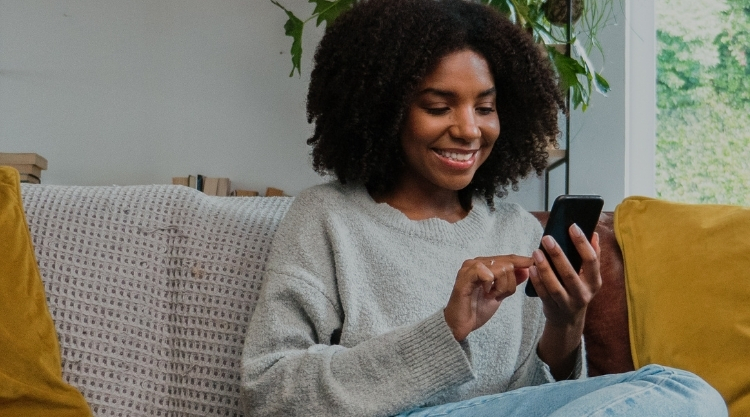 African American woman smiling at home while scrolling on her phone