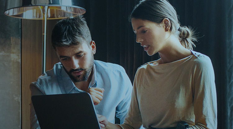 Adult woman pointing at a computer screen and an adult man looking at it while in an office space