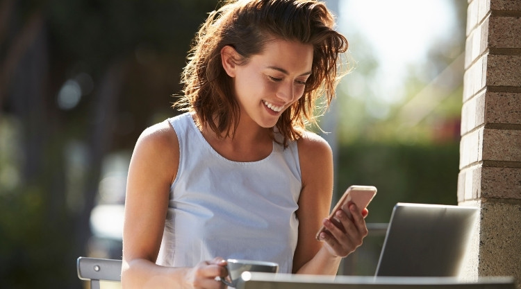 Woman holding coffee mug, looking at phone while smiling