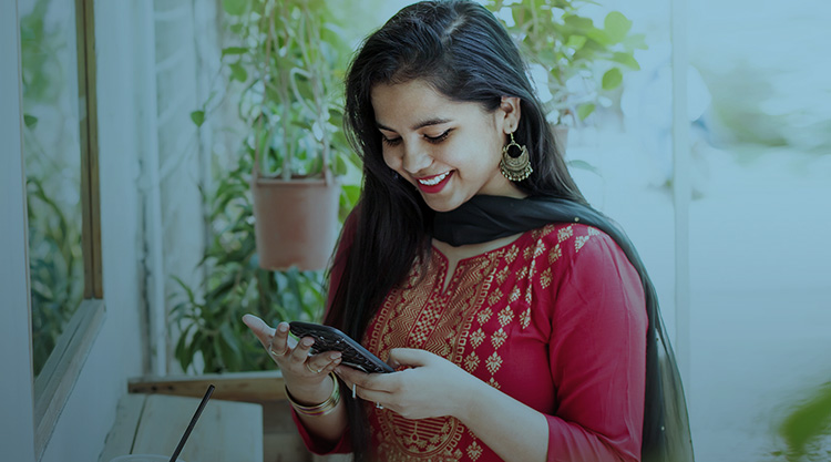 Young woman smiling and looking down at her cell phone with plants behind her