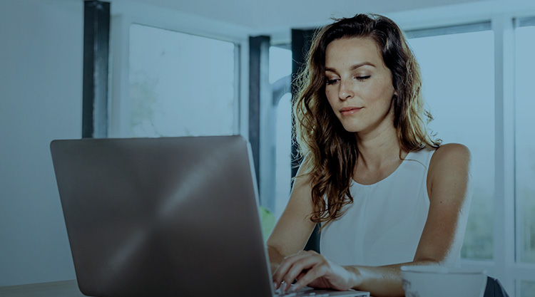 Adult smiling woman typing on her laptop while sitting at a desk and a cup of tea next to her