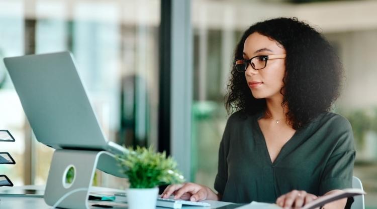 Young woman with dark hair and glasses looking intently at a laptop