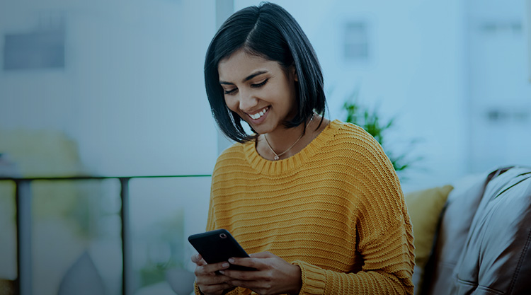 Smiling adult woman looking at a cell phone while sitting down on a couch