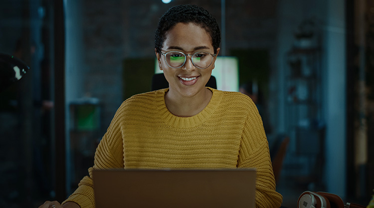 Smiling adult woman sitting at her desk in an office while working on her laptop