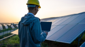 Man wearing hard hat holding a laptop outside at solar farm.
