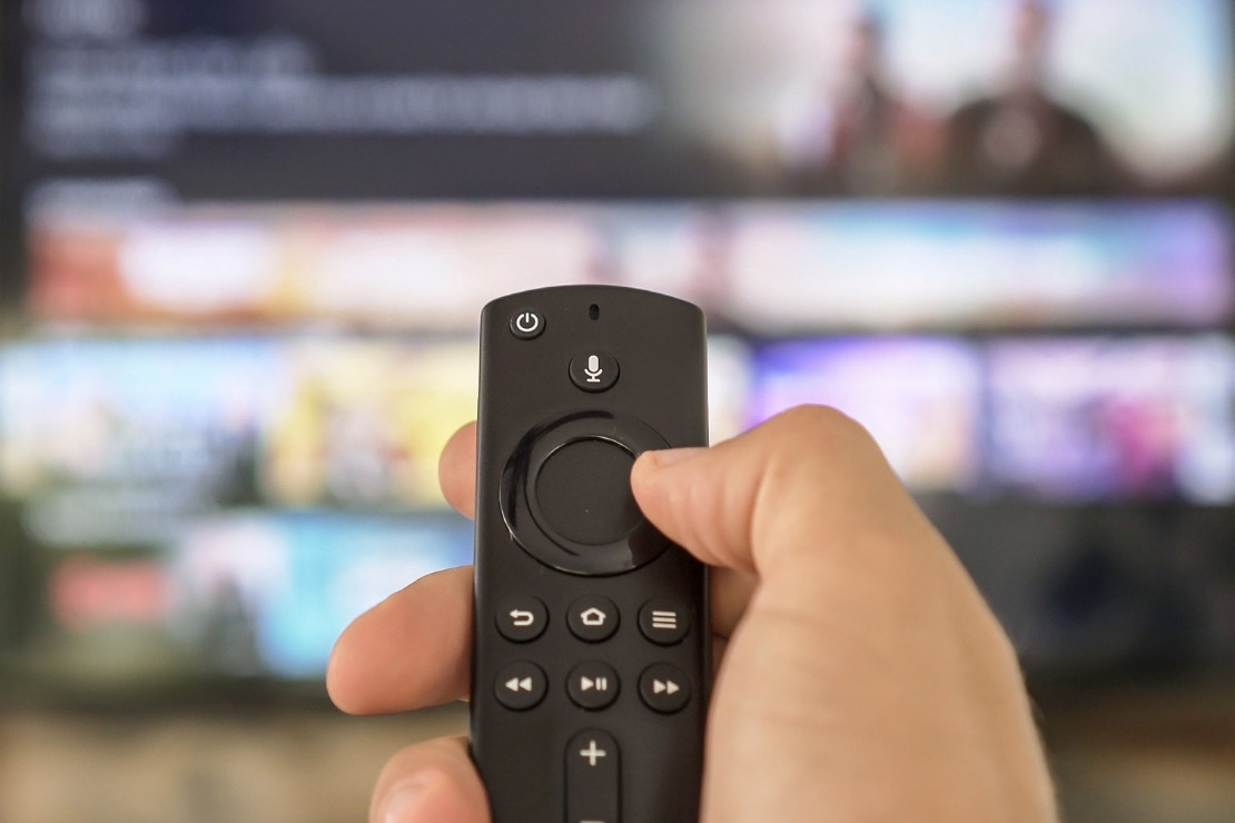 Hand holding a remote pointed at a blurred out tv