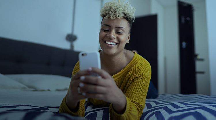 Smiling adult woman laying on the bed while looking at her cell phone