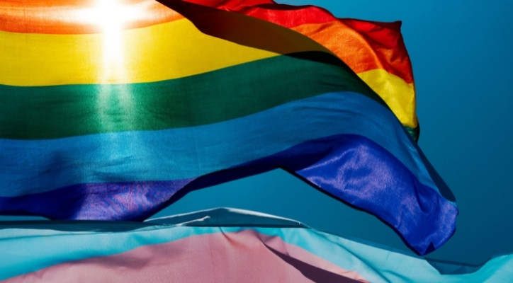 An image of LGBTQ+ pride flag and trans pride flag waving in the wind