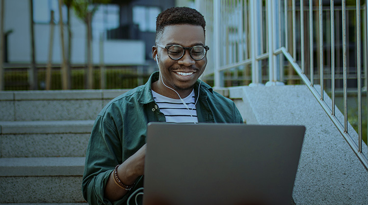 Young man sitting on the stairs in a front of the office building, working using a laptop