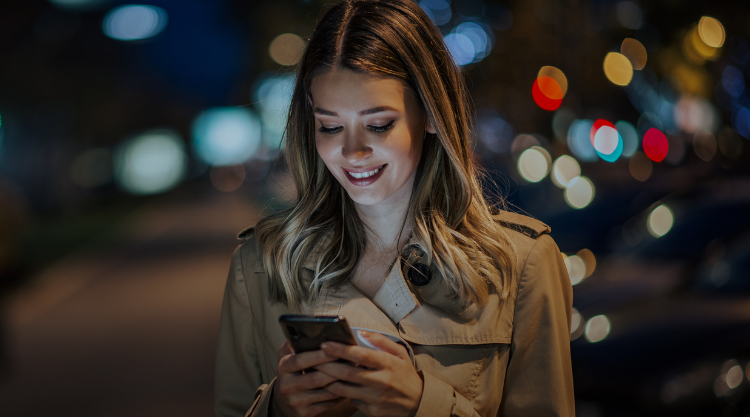 Portrait of a smiling young woman using smart phone at night