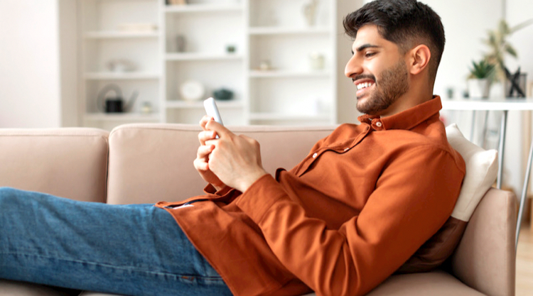 Happy man using his mobile device while reclining