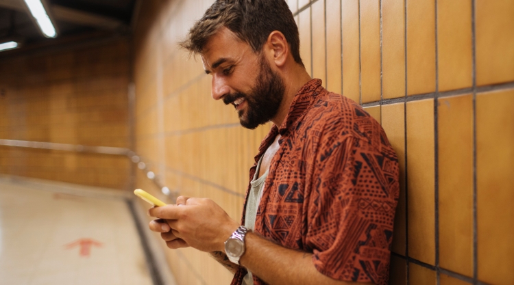 A bearded man smiles as he works on his mobile phone
