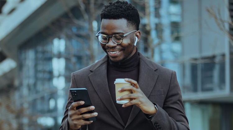 Young handsome african american man wearing brown blazer scrolling his phone while smiling