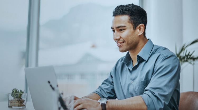 Young south asian man on laptop smiling while working