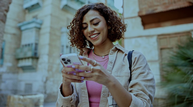 Woman with curly brown hair looking at smart phone and smiling