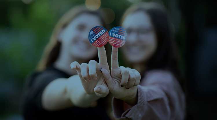 Portrait of two women holding out their hands together with the I voted stickers attached to their fingers for the viewer to see