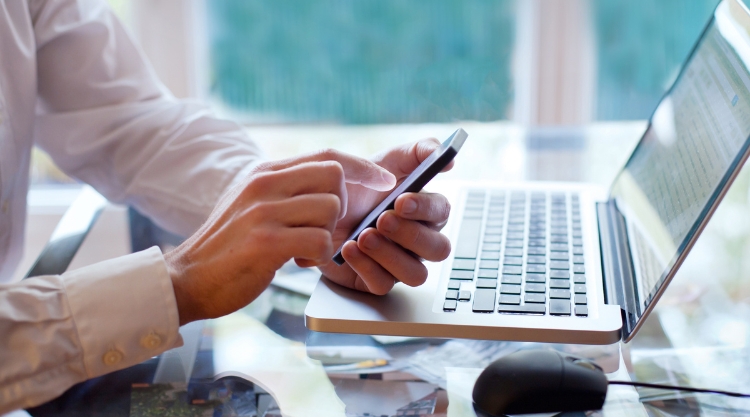 A person take s a break from their laptop computer to check their mobile device